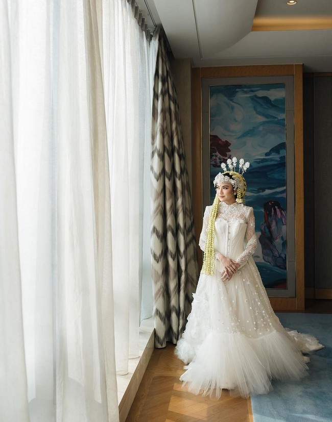 Sebelum mengenakan kebaya akad nikah, Mahalini mengenakan bridal robe mewah bergaya Victorian dari koleksi Lisa Ju. Jubah pengantin ini tampil mewah dengan detail-detail bunga atraktif serta aplikasi bunga tiga dimensi di bagian bawah hem. Foto: Instagram/@axioo @thebridestory @hiantjen