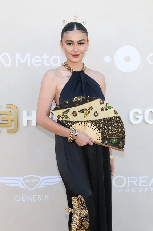Pelantun Get Loose itu muncul dalam balutan gaun panjang hitam polos bersiluet A-line dengan detail rantai emas pada potongan leher bergaya halter itu. Alih-alih clutch, ia menenteng kipas bermotif batik. (Foto: Monica Schipper/GETTY IMAGES NORTH AMERICA/Getty Images via AFP)