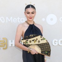 Pelantun Get Loose itu muncul dalam balutan gaun panjang hitam polos bersiluet A-line dengan detail rantai emas pada potongan leher bergaya halter itu. Alih-alih clutch, ia menenteng kipas bermotif batik. (Foto: Monica Schipper/GETTY IMAGES NORTH AMERICA/Getty Images via AFP)