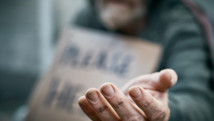 A pathetic homeless man begs on the sidewalk.