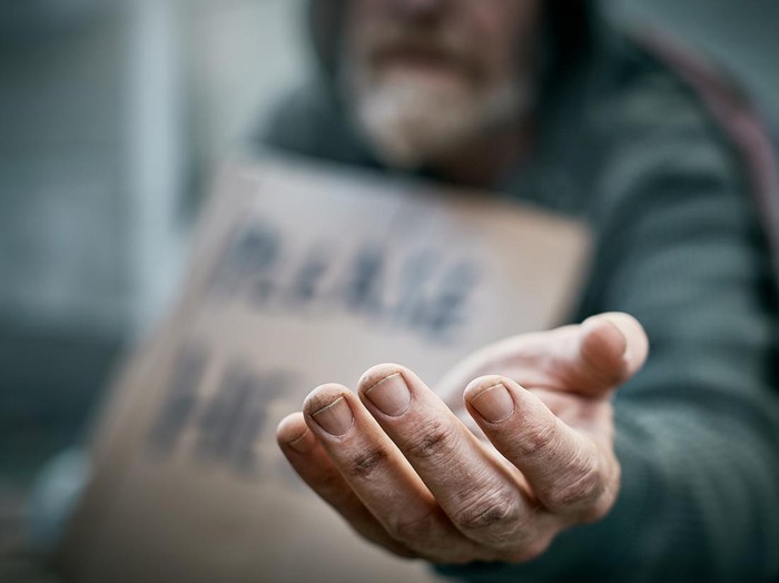 A pathetic homeless man begs on the sidewalk.