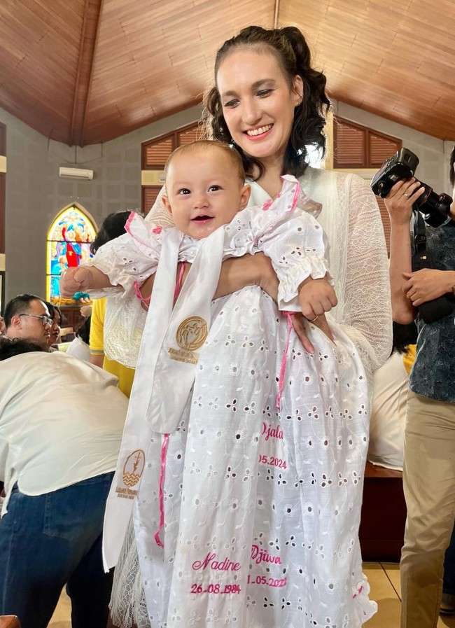 Walaupun masih tampak kebesaran namun baby Djala tampak imut dan menggemaskan mengenakan dress putih tersebut. Sambil digendong sang mama, baby Djala tampak tersenyum. Foto: dok. Instagram/@nadinelist