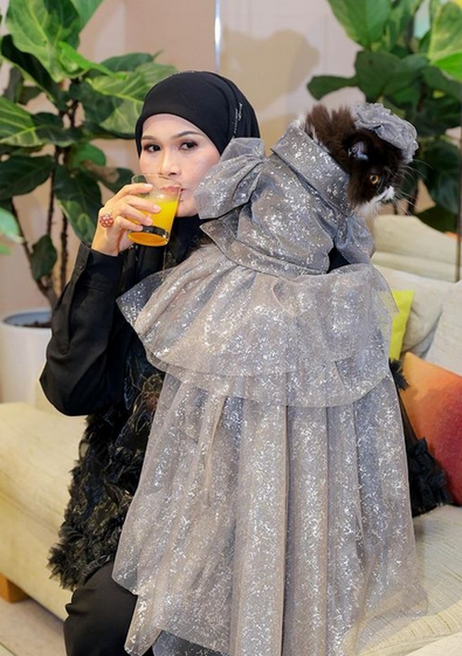 Haliza menggendong kucing yang mengenakan gaun berwarna abu-abu bertahtakan kristal Swarovski rancangan desainer ternama asal Malaysia, Rizalman Ibrahim. Foto: dok. Instagram @Haliza Maysuri