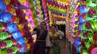 Dengan mengenakan jas hujan, pengunjung festival berjalan menyusuri jalan dengan lentera teratai merah muda dan bunga yang menyala.