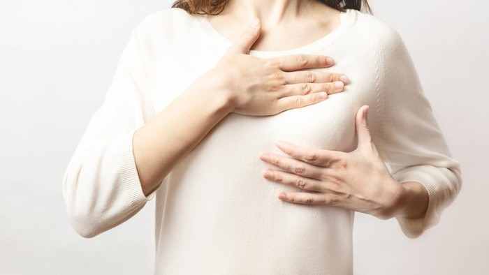 Woman hand checking lumps on her breast for signs of breast cancer on white background. Healthcare concept. Cancer self check; healthy girl.