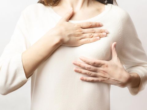 Woman hand checking lumps on her breast for signs of breast cancer on white background. Healthcare concept. Cancer self check; healthy girl.