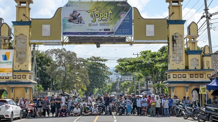 Petugas kepolisian melintas dekat mobil yang dijadikan blokade jalan saat aksi unjuk rasa di jalan wisata Senggigi, Desa Meninting, Kecamatan Batulayar, Lombok Barat, NTB, Rabu (15/5/2024). Ratusan warga melakukan aksi tutup jalan memprotes lambannya penanganan aparat kepolisian terkait penyelesaian kasus penyerangan warga Dusun Montong Buwuh, Desa Meninting oleh massa bersenjata tajam dari luar Lombok Barat pada Jumat (10/5) malam. ANTARA FOTO/Ahmad Subaidi/Spt.