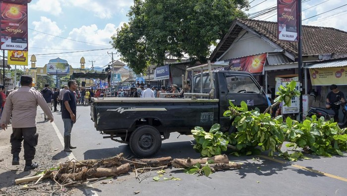 Petugas kepolisian melintas dekat mobil yang dijadikan blokade jalan saat aksi unjuk rasa di jalan wisata Senggigi, Desa Meninting, Kecamatan Batulayar, Lombok Barat, NTB, Rabu (15/5/2024). Ratusan warga melakukan aksi tutup jalan memprotes lambannya penanganan aparat kepolisian terkait penyelesaian kasus penyerangan warga Dusun Montong Buwuh, Desa Meninting oleh massa bersenjata tajam dari luar Lombok Barat pada Jumat (10/5) malam. ANTARA FOTO/Ahmad Subaidi/Spt.