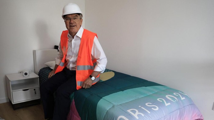 International Olympic Committee (IOC) president Thomas Bach sits on a bed as he visits the Athletes village in Saint-Ouen-sur-Seine, outside Paris, Tuesday, July 25, 2023. (Pascal Rossignol/Pool via AP)