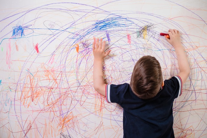 The child draws on the wall with colored chalk. The boy is engaged in creativity at home