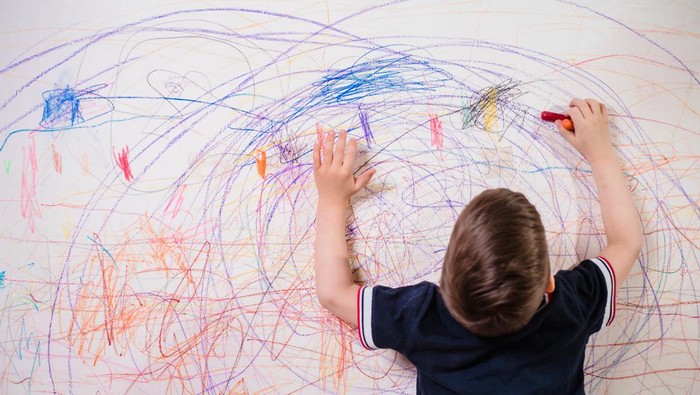 The child draws on the wall with colored chalk. The boy is engaged in creativity at home