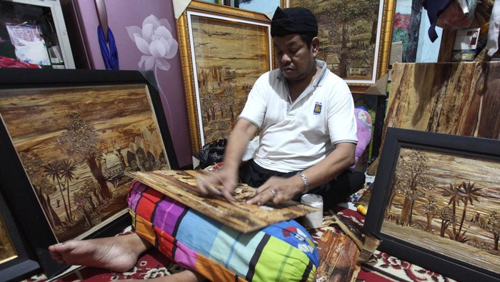 Kreatif! Limbah Pelepah Pisang Diubah Jadi Karya Seni Bernilai Ekonomi Jamaludin (54) membuat lukisan dari pelepah batang pohon pisang di Surabaya, Jawa Timur, Sabtu (18/5/2024). Perajin yang pernah mengalami kecelakaan kerja pada tahun 2008 dan mengakibatkan kelumpuhan pada kakinya itu membuat lukisan berbahan baku dari pelepah batang pohon pisang kering dan dijual ke berbagai daerah dengan harga Rp200 ribu hingga Rp6 juta per lukisan. ANTARA FOTO/Didik Suhartono/wpa.