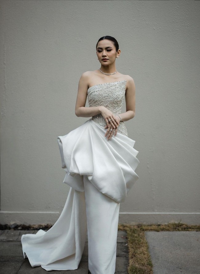 Gaya glamor bak princess kembali jadi pilihan Mahalini untuk resepsi pernikahan di Bali. Hian Tjen menciptakan gaun berwarna putih dengan aksen lipit di pinggang dan bustier penuh hiasan payet dan kristal. Foto: Instagram/@axioo @hiantjen @dhirmanputra