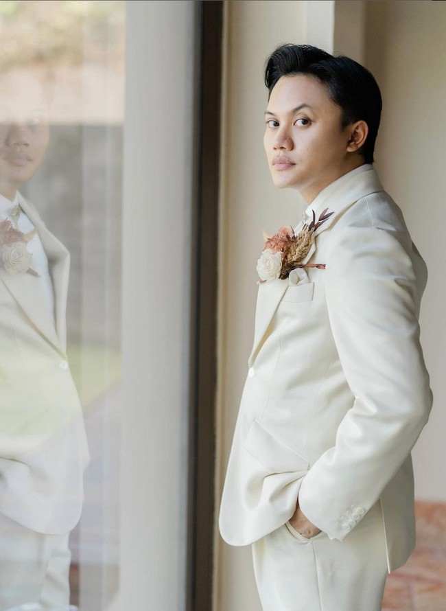 Pengantin pria, Rizky Febian, memilih setelan tuksedo dari koleksi Henri Winata. Tampilannya chic sekaligus elegan dengan padanan warna putih dan ivory. Foto: Instagram/@axioo @hiantjen @dhirmanputra