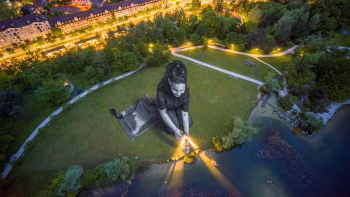 Lukisan Raksasa Gambarkan Penderitaan Para Migran A drone view shows the artwork Bright Dreams by French-Swiss artist Saype, which represents a girl holding a lighthouse pointing to a dingy boat filled with migrants, in support of the humanitarian sea rescue association SOS Mediterranee, in Irchelpark, Zurich, Switzerland, May 12, 2024. The artwork covers an area of 4,500 square meters using biodegradable pigments made of charcoal, chalk, water and milk proteins. REUTERS/Denis Balibouse