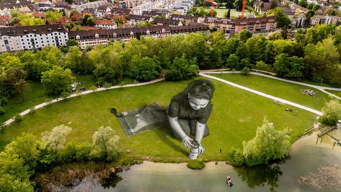 Lukisan Raksasa Gambarkan Penderitaan Para Migran A drone view shows the artwork Bright Dreams by French-Swiss artist Saype, which represents a girl holding a lighthouse pointing to a dingy boat filled with migrants, in support of the humanitarian sea rescue association SOS Mediterranee, in Irchelpark, Zurich, Switzerland, May 12, 2024. The artwork covers an area of 4,500 square meters using biodegradable pigments made of charcoal, chalk, water and milk proteins. REUTERS/Denis Balibouse