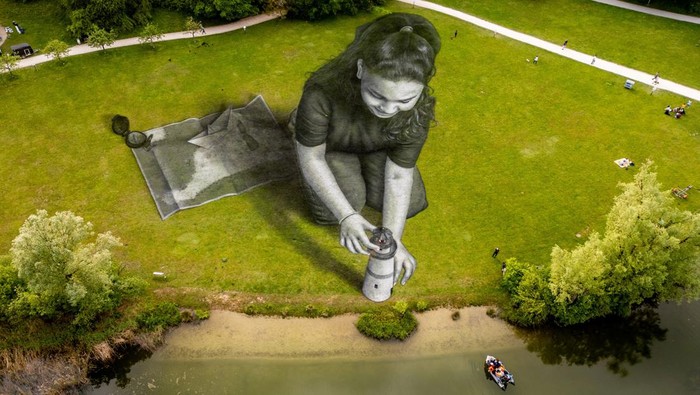 Lukisan Raksasa Gambarkan Penderitaan Para Migran A drone view shows the artwork Bright Dreams by French-Swiss artist Saype, which represents a girl holding a lighthouse pointing to a dingy boat filled with migrants, in support of the humanitarian sea rescue association SOS Mediterranee, in Irchelpark, Zurich, Switzerland, May 12, 2024. The artwork covers an area of 4,500 square meters using biodegradable pigments made of charcoal, chalk, water and milk proteins. REUTERS/Denis Balibouse