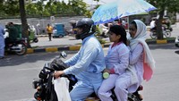 Meski berbahaya, pemotor nekat menjadikan payung untuk melindungi diri dari panas terik matahari. AP Photo/KM Chaudary.