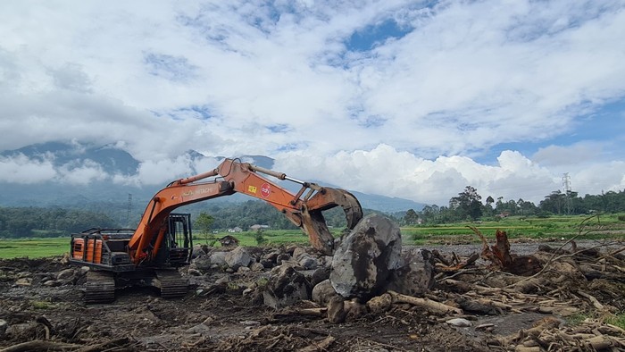 Alat berat dikerahkan guna membersihkan material bebatuan di wilayah Simpang Bukit Batiuah pada Jumat (21/5). Bebatuan ini adalah dampak dari galodo dari Gunung Marapi, Sumbar. (BNPB)