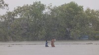 Seorang wanita dan anak-anak mengarungi air saat Topan Remal melanda daerah Shyamnagar, Satkhira, Bangladesh, Senin (27/5/2024). 