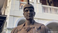 Bergeser ke sebelahnya, berdiri bangunan dua lantai dengan dominasi warna putih dengan gaya da vinci. Di pintu masuknya dijaga oleh dua patung ksatria romawi yang membawa tombak. Untuk naik ke lantai duanya, traveler harus meniti tangga yang disekeliling temboknya dipenuhi foto keluarga besar Rudy J Persik.