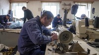 Seorang tawanan perang Rusia menjahit di pusat penahanan. Ukraina secara rutin membuka kamp tawanan perang utamanya bagi Palang Merah, PBB, dan jurnalis internasional. Pada akhir April, The Associated Press mengunjungi lokasi tersebut di bagian barat Ukraina, satu hari penuh perjalanan dari garis depan tempat orang-orang yang berada di dalamnya ditangkap. Kunjungan tersebut dilakukan dengan syarat lokasi tepatnya tidak diungkap.