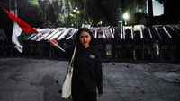 Seorang peserta aksi mengibarkan bendera Palestina di depan barikade polisi.  