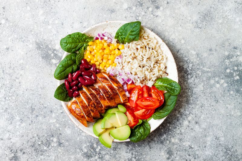 Homemade Mexican chicken burrito bowl with rice, beans, corn, tomato, avocado, spinach. Taco salad lunch bowl