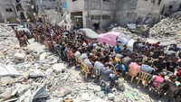 Mereka makan di dekat rumah-rumah yang hancur akibat serangan militer Israel.  