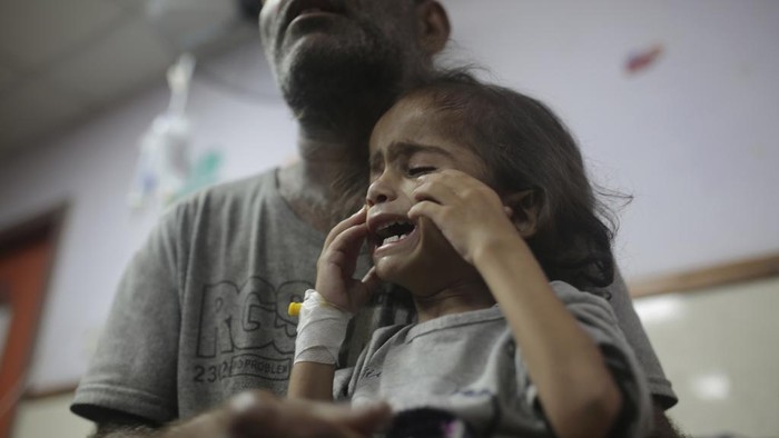 Abdulrahman Al-Rai holds his daughter, Hana Al-Rai, 3, who suffers from diabetes, a weakened immune system, and malnutrition,  as she gets help from her sister to test her blood sugar at Al-Aqsa Martyrs Hospital in Deir al-Balah in the central Gaza Strip, where she is receiving treatment, Saturday, June 1, 2024. The family is displaced from the northern Gaza Strip. (AP Photo/Jehad Alshrafi)