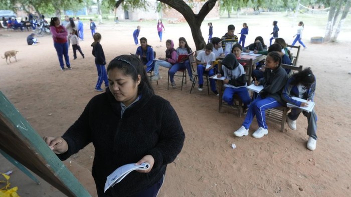 Municipal worker Gloria Soilan teaches seventh graders from the New Asuncion school, outside their school building in Presidente Hayes in Paraguay's Chaco region, Monday, June 3, 2024. Due to not enough classrooms, students have been attending classes outside for the past three years with instruction from a municipal worker. (AP Photo/Jorge Saenz)