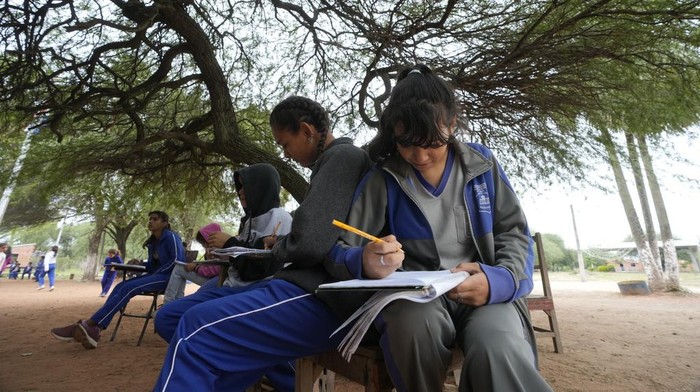 Municipal worker Gloria Soilan teaches seventh graders from the New Asuncion school, outside their school building in Presidente Hayes in Paraguay's Chaco region, Monday, June 3, 2024. Due to not enough classrooms, students have been attending classes outside for the past three years with instruction from a municipal worker. (AP Photo/Jorge Saenz)