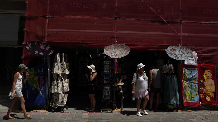 Siprus Dilanda Gelombang Panas, Suhu Mencapai 42 Derajat Celsius A woman walks outside from a souvenir shop as she protects herself from the sun with an umbrella during a hot day in central capital Nicosia, Cyprus, on Tuesday, June 4, 2024. The Meteorological Department said the heatwave's highest temperatures in this days they're expected to reach 42 degrees Celsius (107,6 Fahrenheit) inland and 32 degrees (89,6 Fahrenheit) in the island's main Troodos mountain range. (AP Photo/Petros Karadjias)