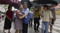 Mereka mengenakan payung saat mengantarkan dan menunggu anak mereka ujian masuk perguruan nasional.