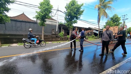 Polisi dan petugas dampar membersihkan tumpahan oli di Jalan Tulikup, Gianyar, Sabtu (8/6/2024).