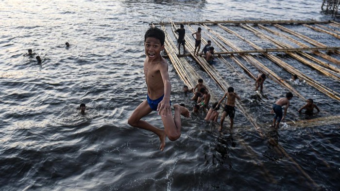 Sejumlah anak mandi di laut kawasan Cilincing, Jakarta Utara. Dengan wajah ceria, mereka berlomba-lomba melompat dari tanggul ke laut.