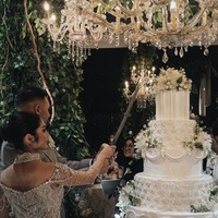 Untuk kue pengantinnya Marco dan Debi memilih kue berwarna putih dengan 5 tingkat. Sesuai dengan tema resepsi pernikahan, kue tersebut juga dihiasi dengan bunga-bunga artificial berwarna senada. Foto: Instagram