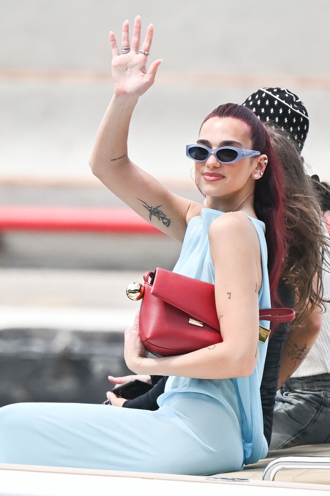 Dua Lipa, yang kini tampil dengan rambut cherry-red, melengkapi busananya dengan sepatu ankle strap hitam, kacamata hitam dan tas tangan merah. Foto: Jacopo Raule/Getty Images