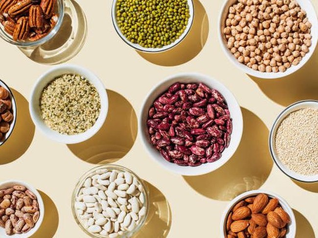 Various kinds of vegan protein sources on beige background. Set of food supplements. Gluten free cereals as ground hemp seeds, quinoa. Nuts and legumes (green mung beans, chick-pea, red lentil, kidney bean, almonds, hazelnuts). Flat lay, top view