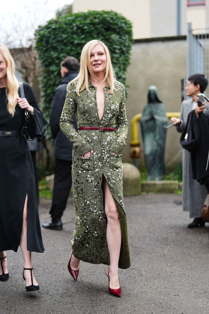 MILAN, ITALY - FEBRUARY 23: Kirsten Dunst wears a green low-neck shiny sequined knitted ribbed wool cardigan worn as a long slit dress, a burgundy thin leather belt, pointed shoes, outside Gucci, during the Milan Fashion Week - Womenswear Fall/Winter 2024-2025 on February 23, 2024 in Milan, Italy. (Photo by Edward Berthelot/Getty Images)