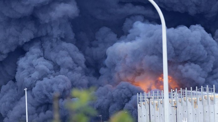 A firefighter, right, works on a ladder truck as a fire rages on the roof of a commercial building at Brussels cargo airport in Brussels, Thursday, June 13, 2024. Firefighters from several municipalities were fighting the fire into the afternoon, no injuries were yet reported. (AP Photo/Virginia Mayo)