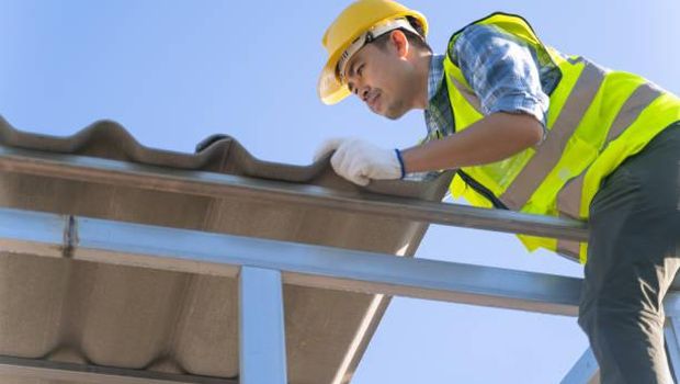 Ilustrasi atap spandek. Male Asian Construction worker installing roof tiles at construction site