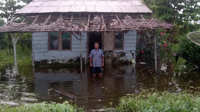 Seorang warga Transmigran Maidi, Kecamatan Oba Selatan, Kota Tidore Kepulauan berpose di depan rumahnya yang tergenang banjir.