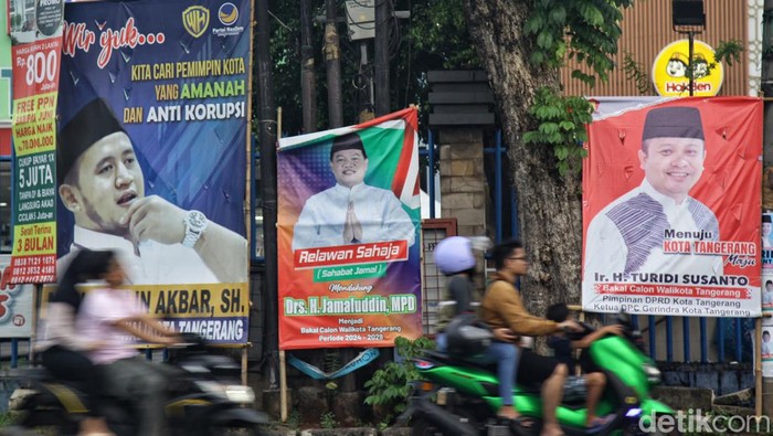Warga melintas di depan spanduk bakal calon kepala daerah di kawasan Ciledug, Kota Tangerang, Banten, Selasa (18/6/2024).