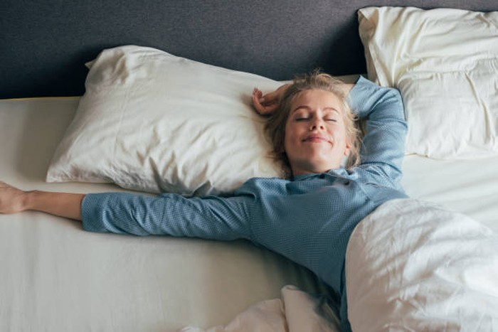Smiling young woman stretching her arms in bed on a sunny morning.