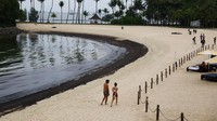 Orang-orang berjalan di samping lapisan minyak di Pantai Tanjong di Sentosa, Singapura. Pada Minggu (16/6), Singapura menutup beberapa taman pantai yang populer karena tumpahan minyak terus menyebar di sepanjang pantainya, dan pihak berwenang berjanji untuk mengintensifkan upaya pembersihan.