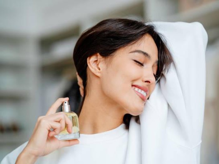 Smiling and joying bob haired woman applying spraying perfume bottle as essential oil on the neck