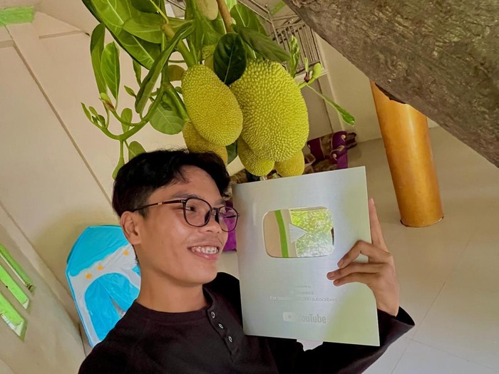 Ardiansyah berfoto di depan pohon nangka sembari memegang silver button dari YouTube.