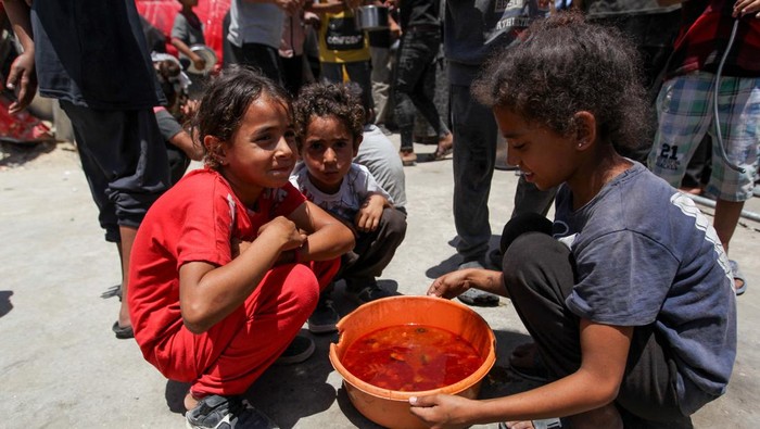 Children look on as Palestinians gather to receive food cooked by a charity kitchen, amid shortages of aid supplies, as the conflict between Israel and Hamas continues, in Khan Younis, in the southern Gaza Strip, June 19, 2024. REUTERS/Hatem Khaled