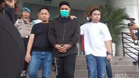 Ia tampak mengenakan hoodie dan topi hitam serta masker.